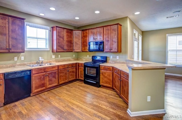 kitchen with black appliances, sink, kitchen peninsula, plenty of natural light, and light wood-type flooring