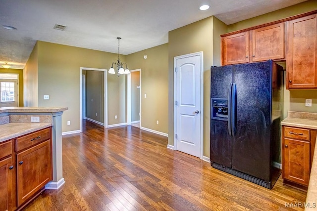 kitchen with black fridge, dark hardwood / wood-style floors, pendant lighting, and a notable chandelier