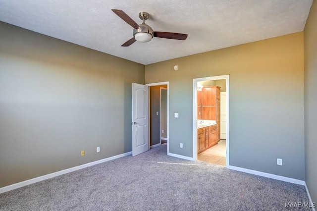 unfurnished bedroom featuring light colored carpet, a textured ceiling, ceiling fan, and ensuite bath