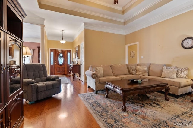 living room featuring hardwood / wood-style flooring, ornamental molding, a raised ceiling, and decorative columns