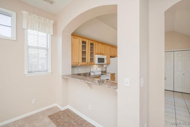 kitchen with lofted ceiling, light tile patterned floors, light stone counters, light brown cabinets, and white appliances