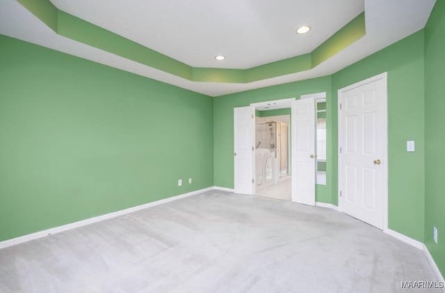 unfurnished bedroom featuring a raised ceiling, connected bathroom, and light colored carpet