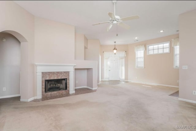 unfurnished living room with ceiling fan, light colored carpet, and a tiled fireplace