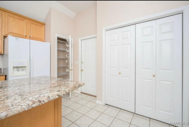 kitchen featuring light stone counters, white refrigerator with ice dispenser, and light tile patterned floors