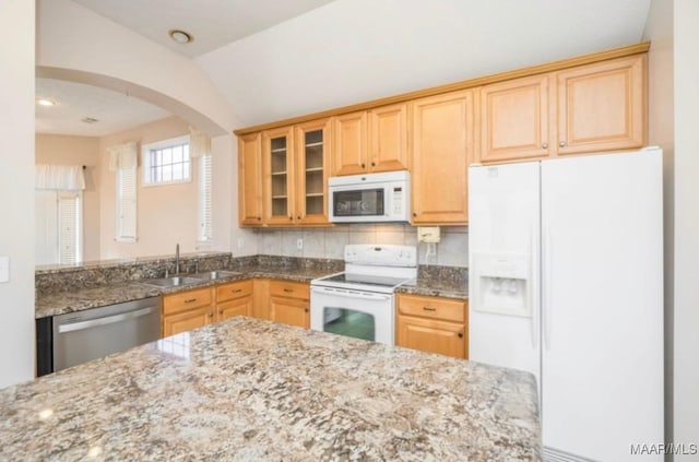 kitchen featuring sink, white appliances, light stone counters, light brown cabinetry, and vaulted ceiling