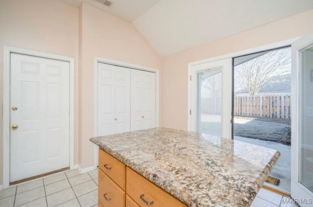 kitchen with lofted ceiling, a center island, light tile patterned floors, and light stone counters