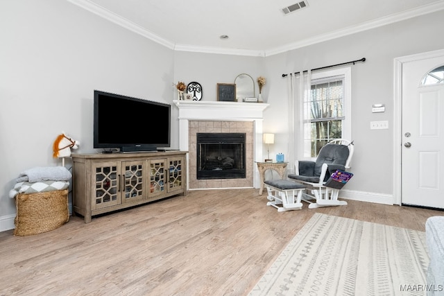 living room featuring hardwood / wood-style flooring, crown molding, and a tile fireplace