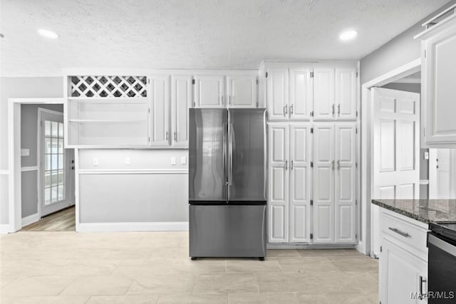 kitchen featuring white cabinetry, a textured ceiling, stainless steel refrigerator, and dark stone countertops