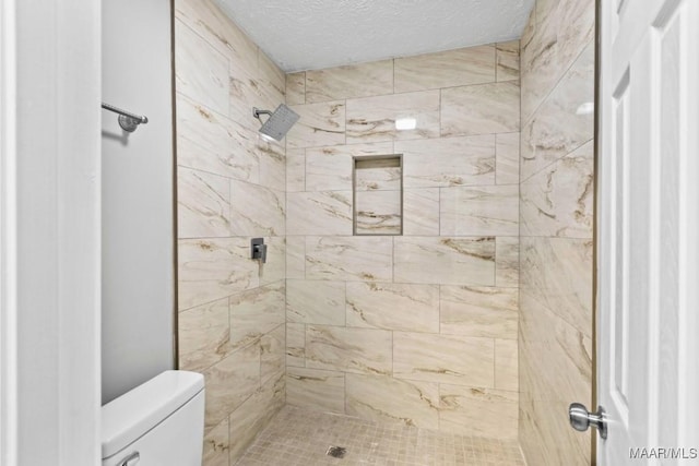 bathroom featuring a tile shower, a textured ceiling, and toilet