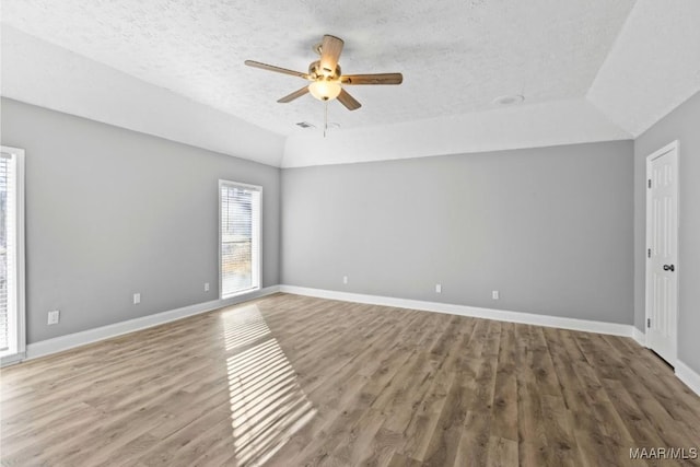 empty room featuring vaulted ceiling, a textured ceiling, a raised ceiling, ceiling fan, and hardwood / wood-style floors