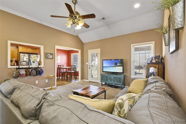 carpeted living area featuring lofted ceiling, ornamental molding, baseboards, visible vents, and a ceiling fan