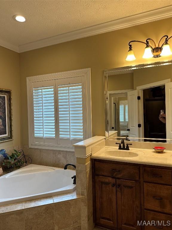 bathroom featuring a relaxing tiled tub, ornamental molding, vanity, and a textured ceiling