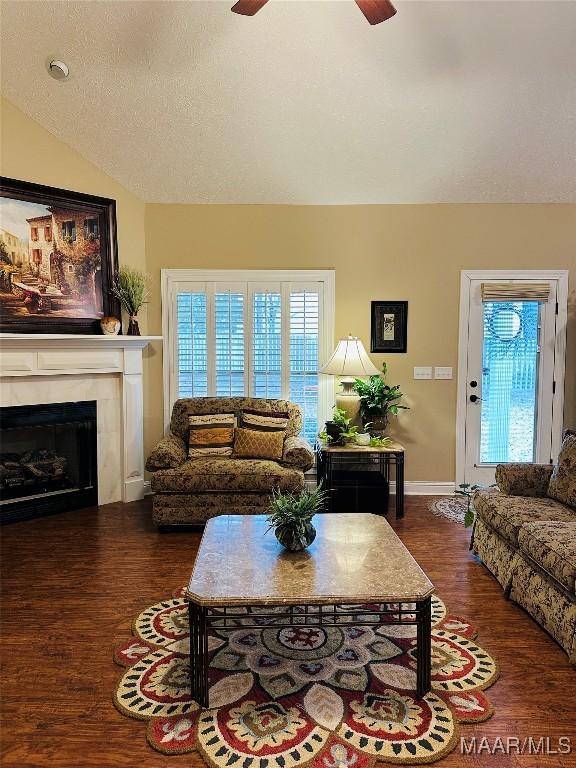 living room with a tiled fireplace, lofted ceiling, dark wood-type flooring, and ceiling fan