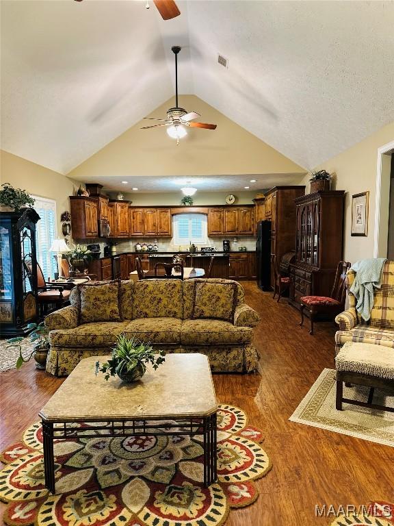 living room with lofted ceiling, dark wood-type flooring, a textured ceiling, and ceiling fan