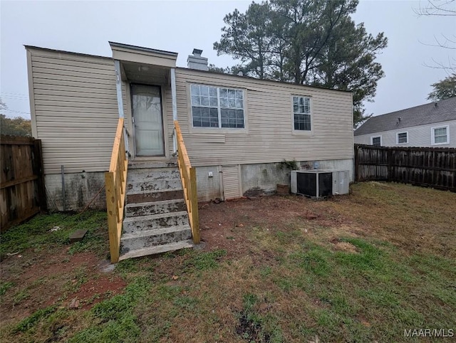 rear view of house featuring cooling unit and a lawn