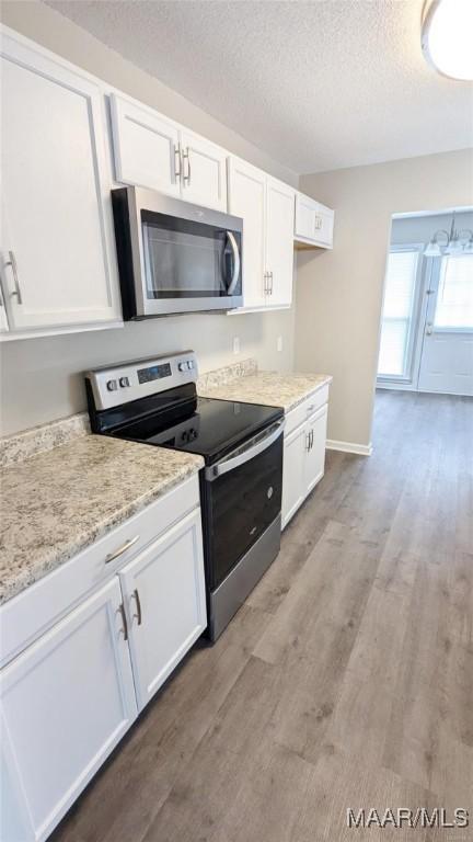 kitchen with white cabinetry, a textured ceiling, light wood-type flooring, appliances with stainless steel finishes, and light stone countertops