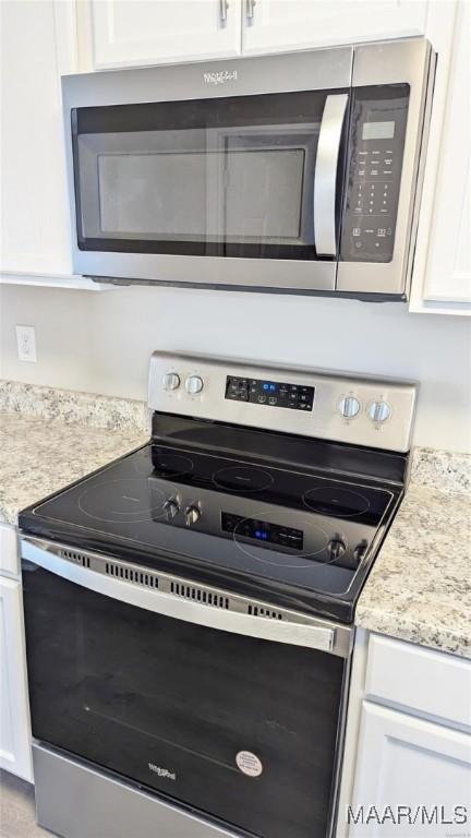 details with white cabinetry, stainless steel appliances, light stone countertops, and a mail area