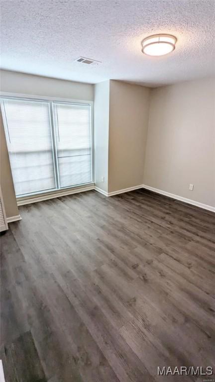 unfurnished room featuring dark wood-type flooring and a textured ceiling