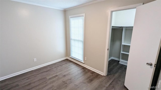 unfurnished bedroom with ornamental molding, a spacious closet, dark wood-type flooring, and a closet