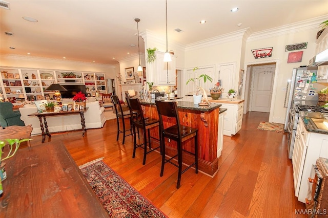 kitchen featuring a center island, stainless steel range with gas stovetop, ornamental molding, a kitchen bar, and decorative light fixtures