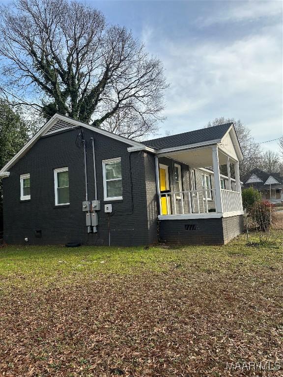 view of side of home featuring covered porch and a lawn