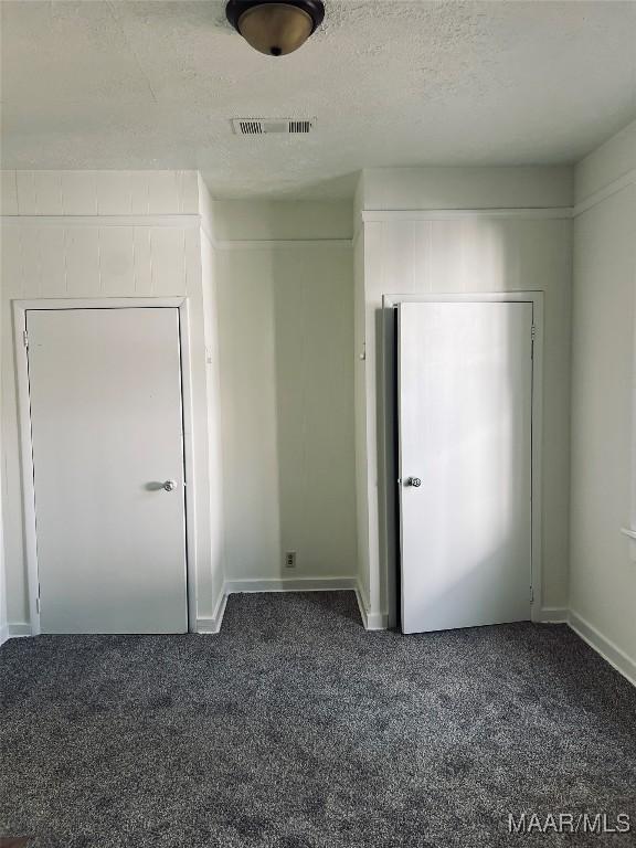 unfurnished bedroom with dark colored carpet and a textured ceiling