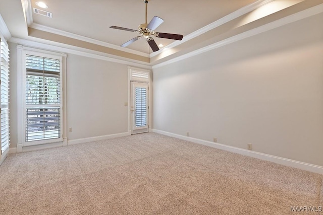 carpeted empty room with ornamental molding, a raised ceiling, visible vents, and baseboards