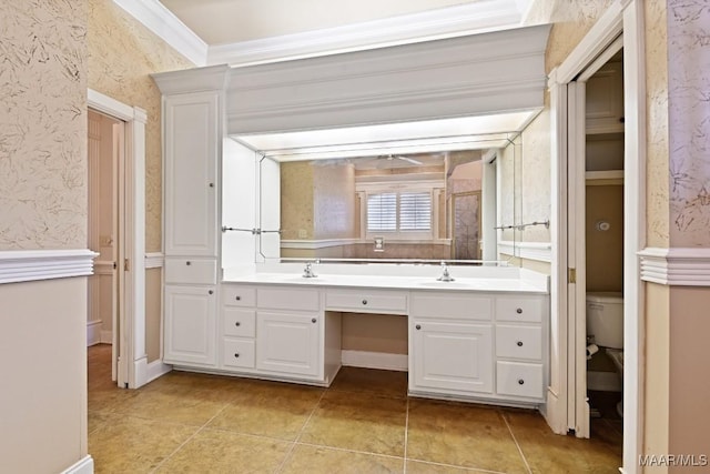 full bath with double vanity, wallpapered walls, toilet, crown molding, and a sink