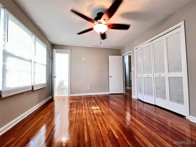 unfurnished bedroom featuring dark wood-type flooring, ceiling fan, connected bathroom, and a closet