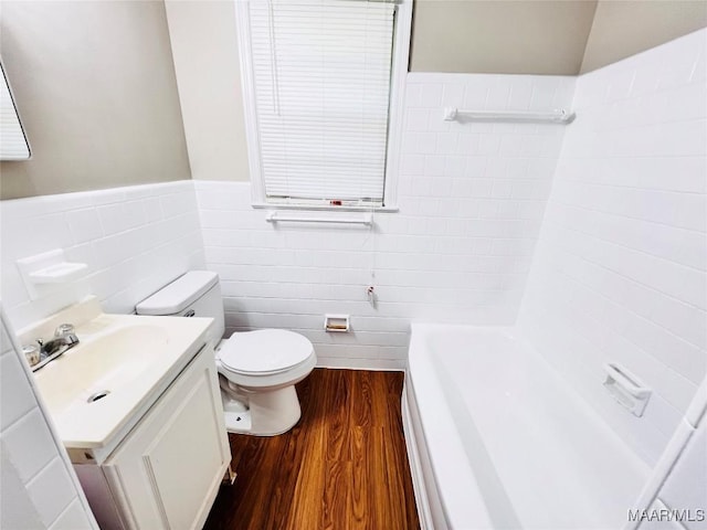 bathroom featuring tile walls, a tub to relax in, hardwood / wood-style flooring, vanity, and toilet