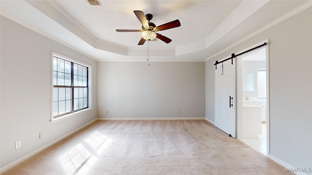 carpeted empty room with a tray ceiling, ornamental molding, a barn door, and ceiling fan