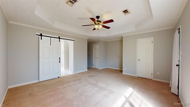 unfurnished bedroom with ceiling fan, a raised ceiling, crown molding, a barn door, and light carpet