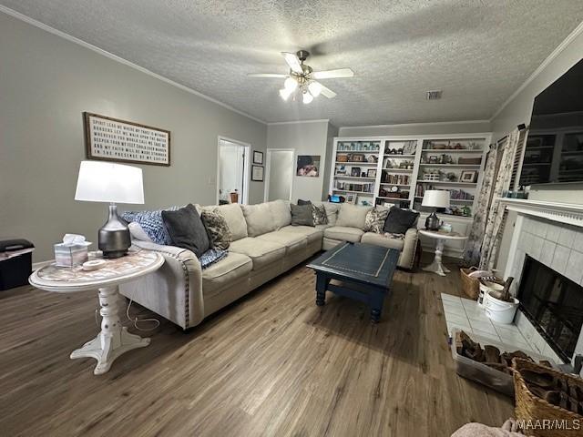 living room featuring built in shelves, a textured ceiling, ornamental molding, hardwood / wood-style flooring, and a fireplace