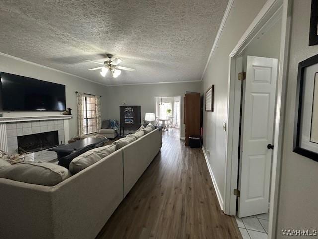 living room featuring ceiling fan, hardwood / wood-style floors, ornamental molding, a textured ceiling, and a tiled fireplace