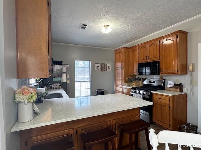 kitchen with sink, a breakfast bar area, stainless steel gas range oven, a textured ceiling, and kitchen peninsula