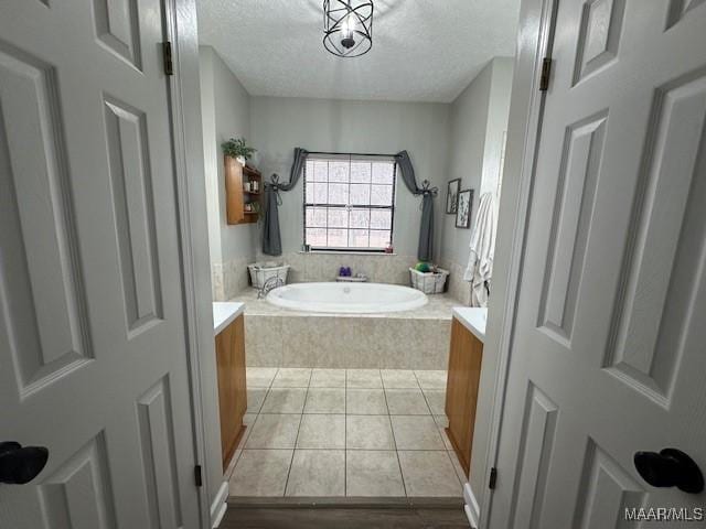 bathroom with vanity, a relaxing tiled tub, tile patterned floors, and a textured ceiling