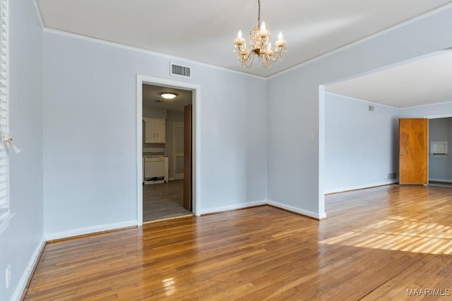 spare room featuring wood-type flooring, an inviting chandelier, and crown molding