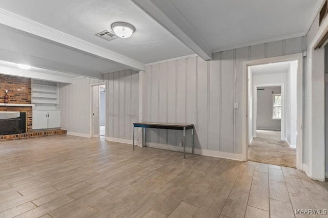 unfurnished living room featuring built in features, a fireplace, beam ceiling, crown molding, and light wood-type flooring