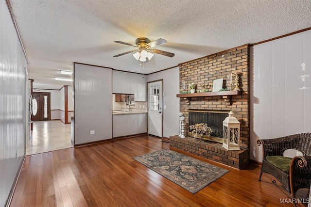 living room featuring a brick fireplace, hardwood / wood-style flooring, a textured ceiling, and ceiling fan