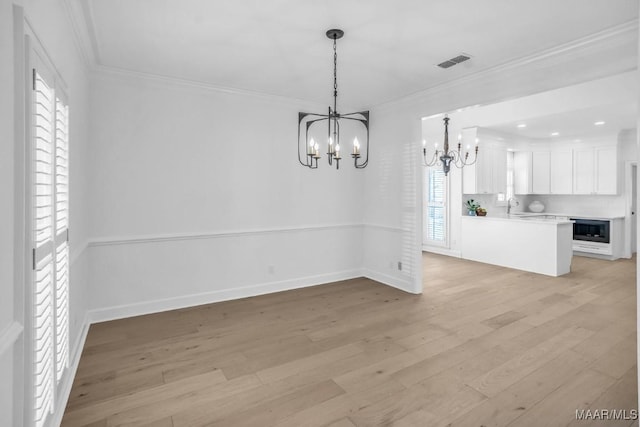 unfurnished dining area with an inviting chandelier, ornamental molding, sink, and light hardwood / wood-style floors