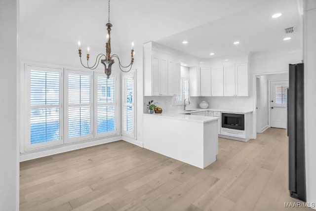 kitchen featuring sink, kitchen peninsula, white cabinets, pendant lighting, and black appliances