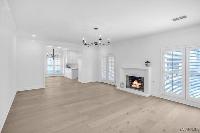 unfurnished living room with an inviting chandelier, crown molding, and light hardwood / wood-style floors