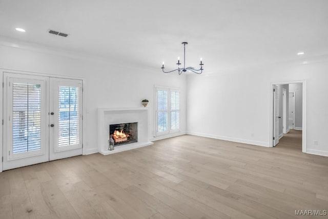 unfurnished living room with french doors, crown molding, light hardwood / wood-style floors, and a notable chandelier