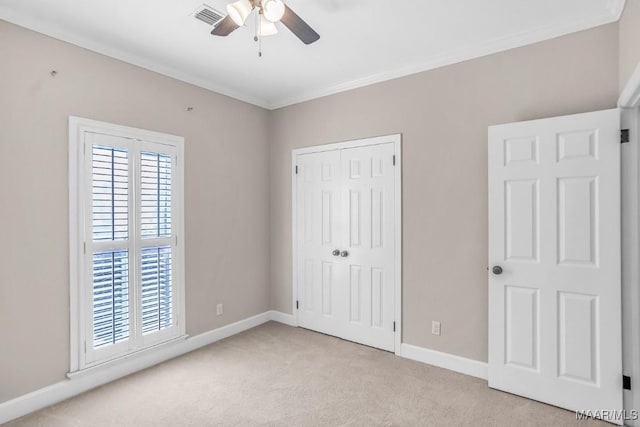 unfurnished bedroom featuring crown molding, ceiling fan, a closet, and light carpet