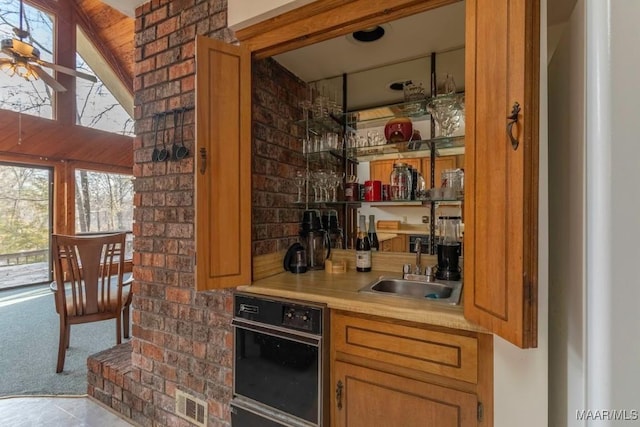 bar featuring ceiling fan, oven, sink, and light carpet