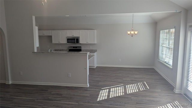 kitchen with pendant lighting, appliances with stainless steel finishes, white cabinetry, light stone counters, and a chandelier