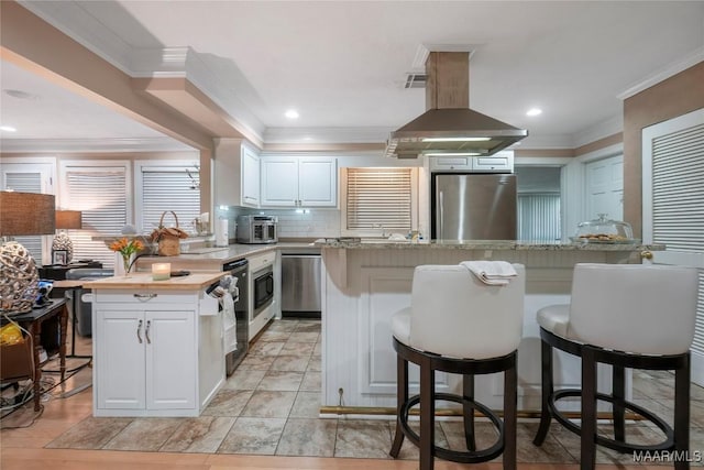 kitchen with white cabinetry, island range hood, appliances with stainless steel finishes, a kitchen island, and decorative backsplash