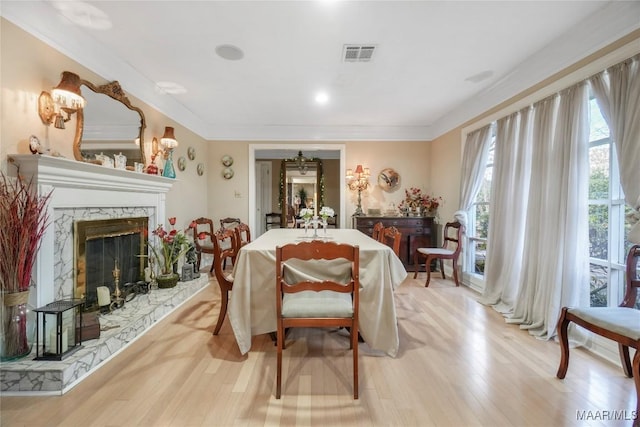 dining area with light hardwood / wood-style flooring, ornamental molding, and a premium fireplace