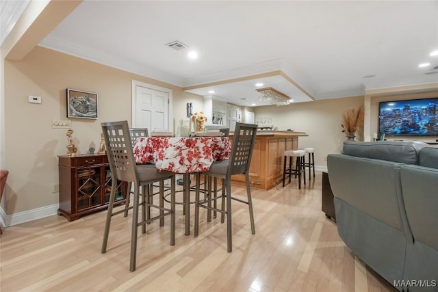 dining space featuring bar, ornamental molding, and light hardwood / wood-style flooring