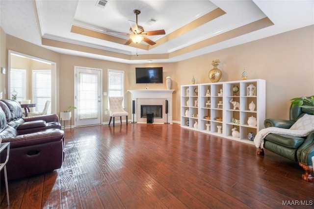 living room featuring hardwood / wood-style flooring, ornamental molding, ceiling fan, and a tray ceiling